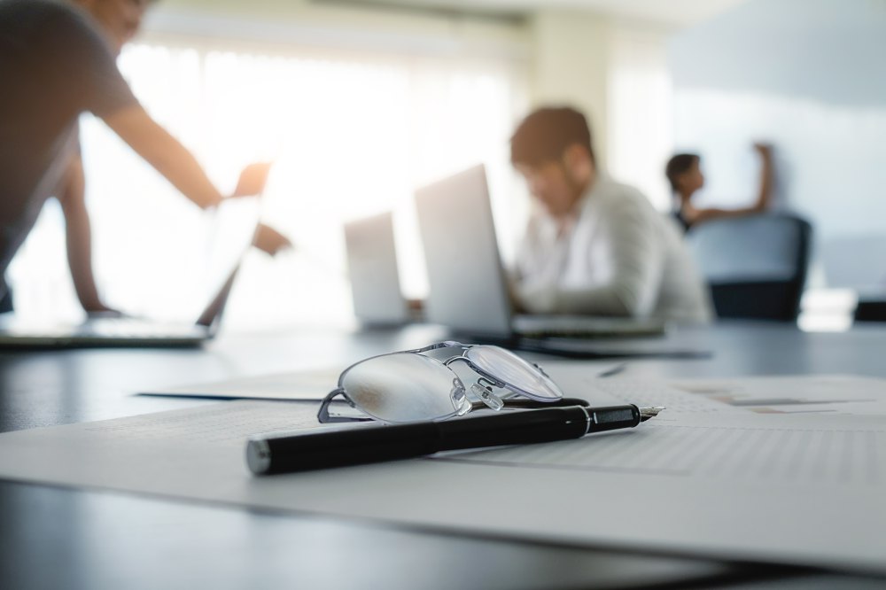 Schreibtisch mit Brille, Stift und Unterlagen in einem ruhigen Büro