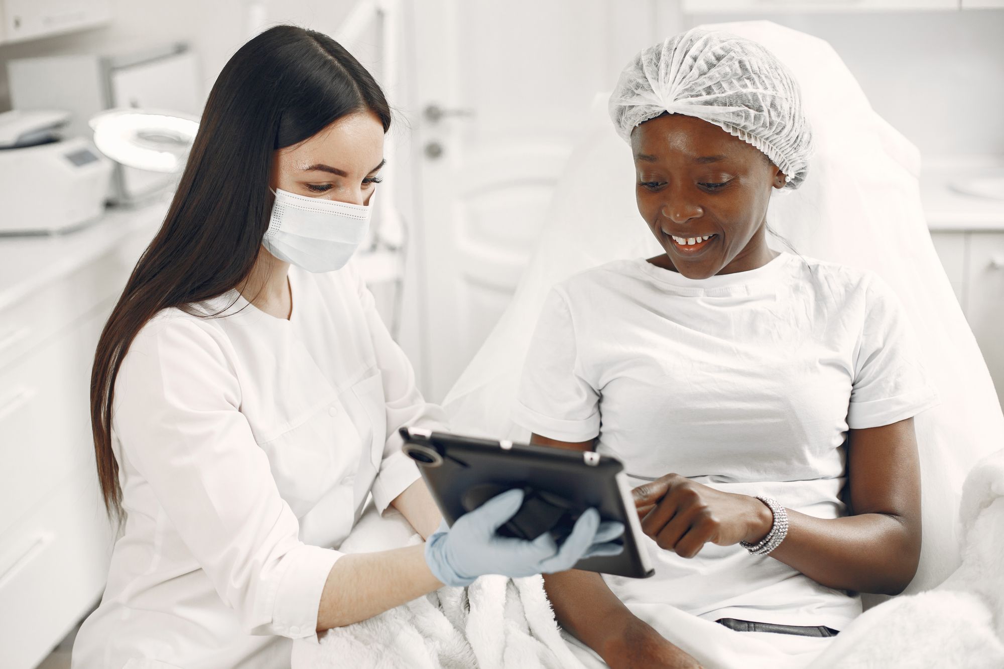 Ärztin zeigt einer Patientin auf der Behandlungsliege Informationen auf einem Tablet