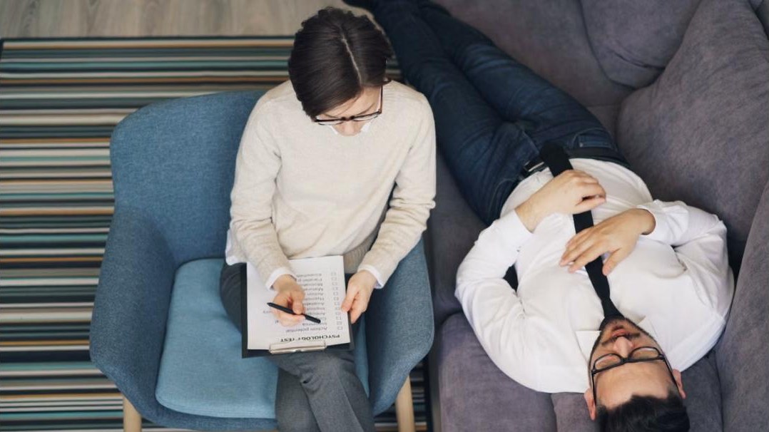 Therapeutisches Gespräch: Ärztin mit Notizen und Patient auf dem Sofa